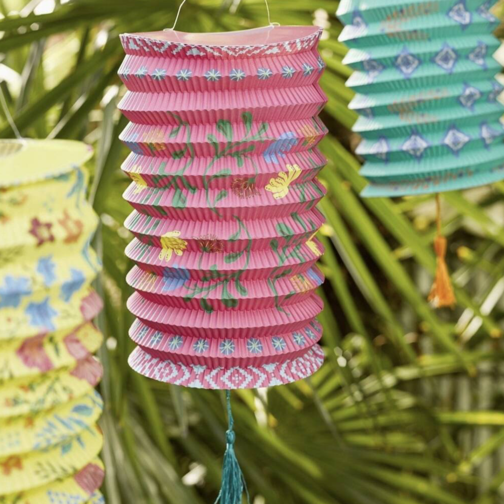 Close up of the pink boho paper lantern with butterfly and floral print hanging against palm leaves