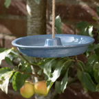 Ceramic Hanging Bird Feeder and Bath in blush pink hanging from a jute rope among green garden foliage