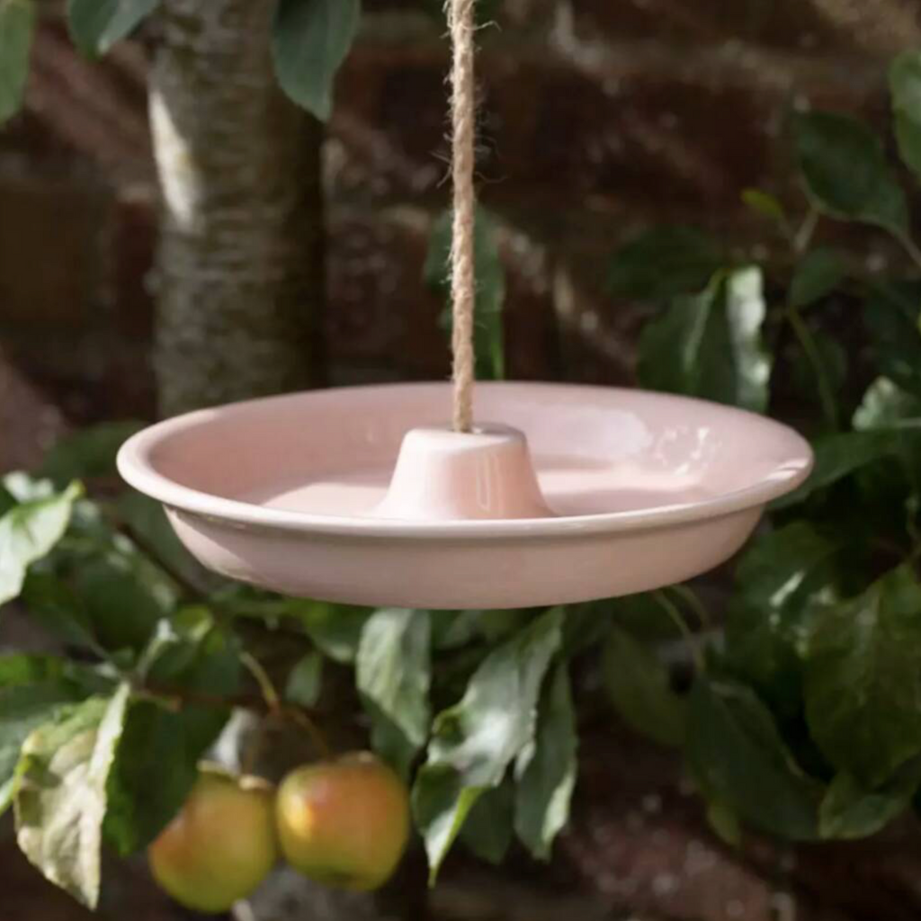 Cornflower blue Ceramic Hanging Bird Feeder and Bath hanging from a jute rope in a garden with apple tree in background