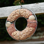 Bird Food Wreath hanging from a rope against a mossy stone wall in a garden with green foliage