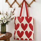 Close up of Recycled Hearts Shopping Bag leaning against a white panelled wall with white daisies and red flowers in background