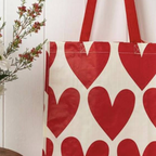 Recycled Hearts Shopping Bag hanging from a wooden wall hook next to white daisies and red flowers in a green vase