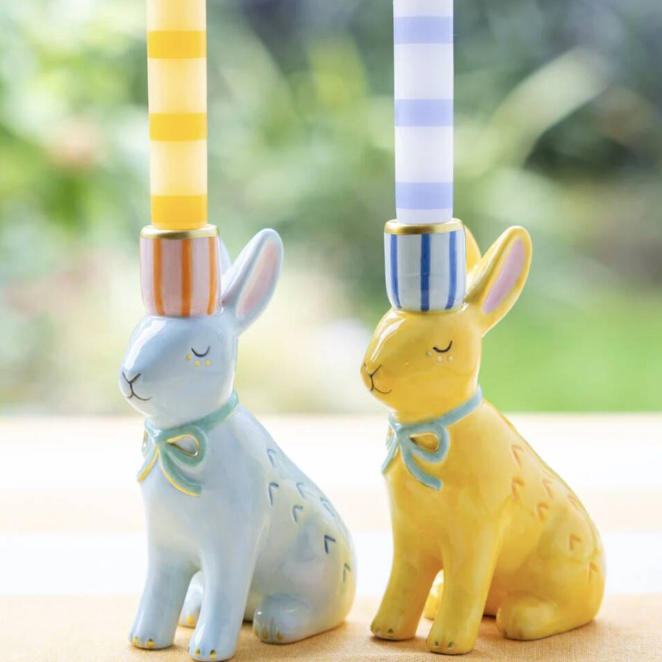 Hand Painted Bunnies Ceramic Candle Holder pair styled on a wooden surface with yellow stripe and blue gingham dinner candles lit against a garden window