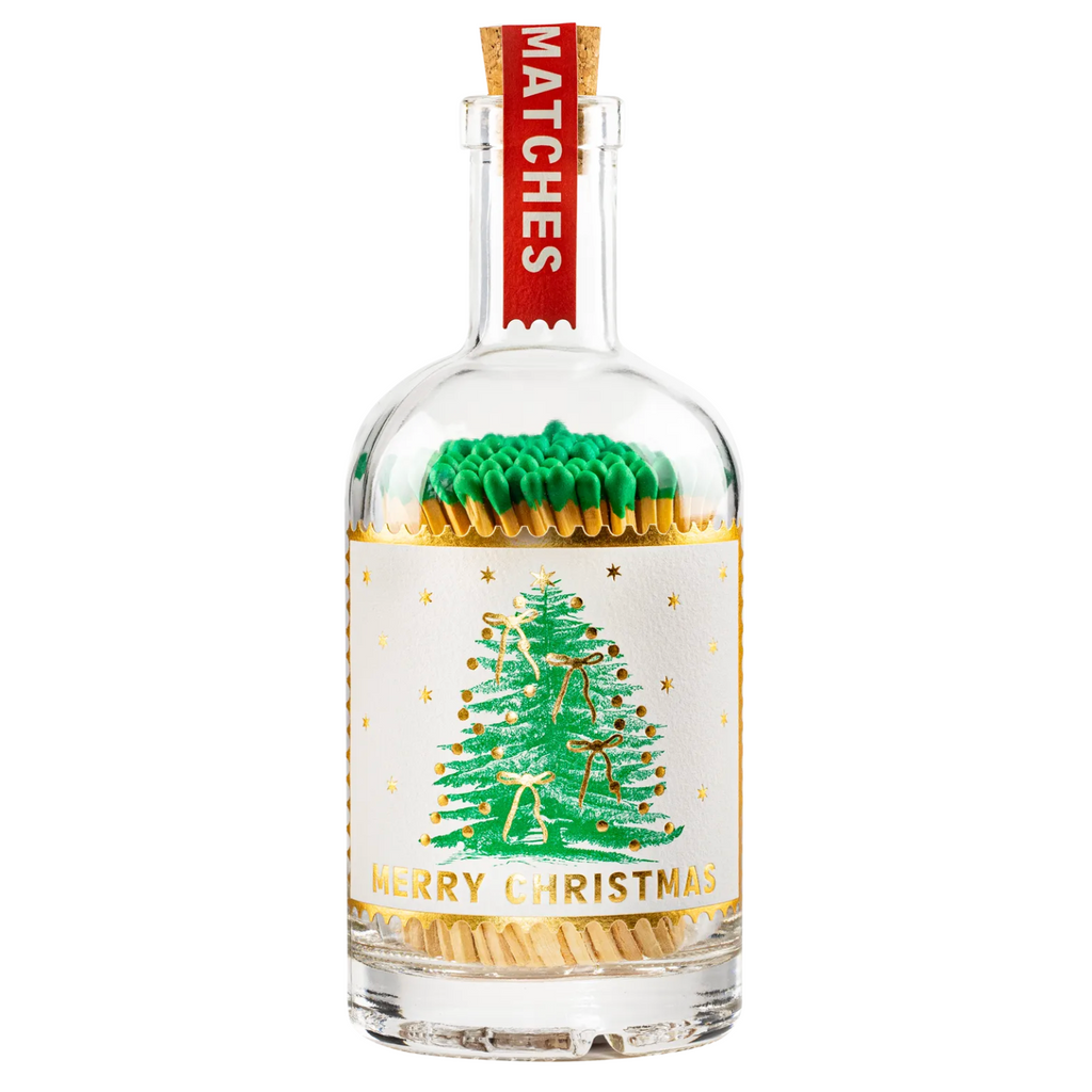Personalised Christmas Match Bottle held in two hands in a cosy cream knit sweater beside a Christmas tree showing the personalised wooden tag reading Merry Xmas Hannah Hope this warms you up Lots of Love Mum