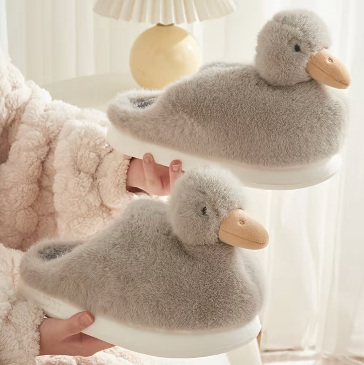 Grey duckling slippers with soft fluffy texture and duck faces held in hand