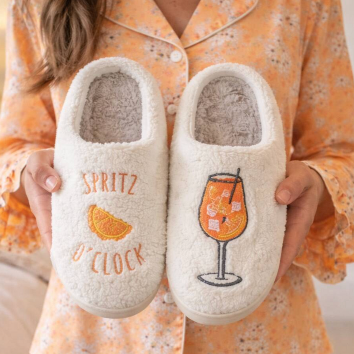 Cream Spritz O’Clock slippers with orange cocktail embroidery held up for display