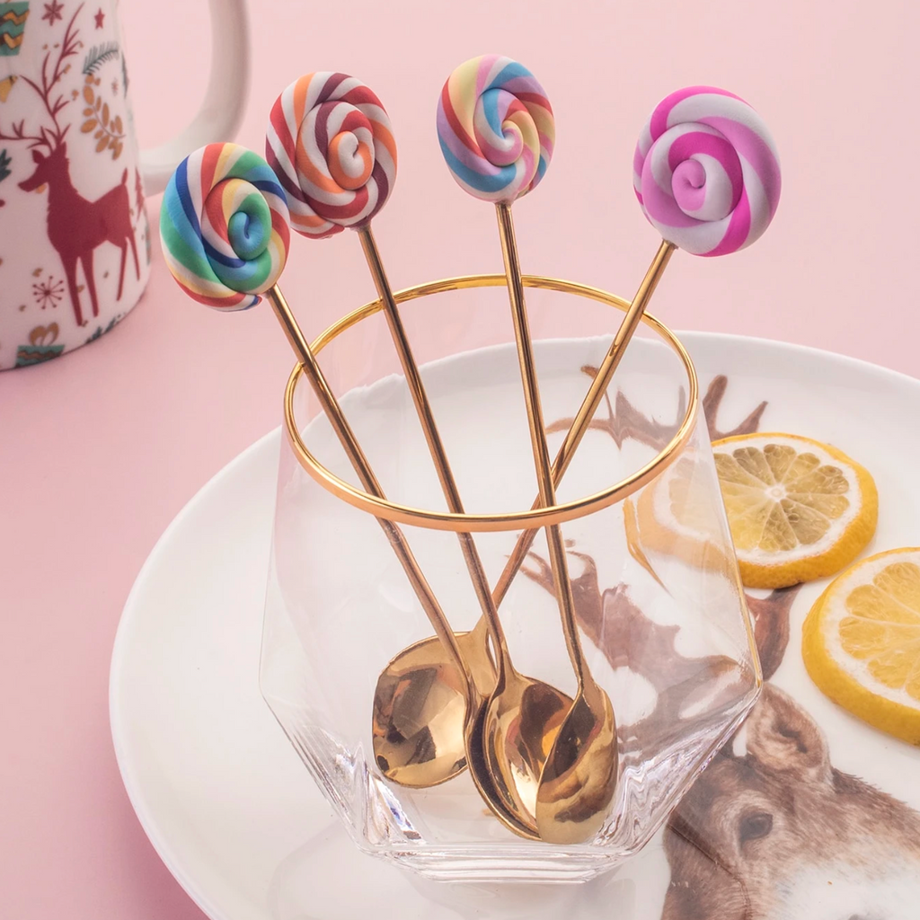 Four gold lollipop cutlery pieces arranged in a glass beside a dessert setting