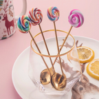 Four gold lollipop cutlery pieces arranged in a glass beside a dessert setting
