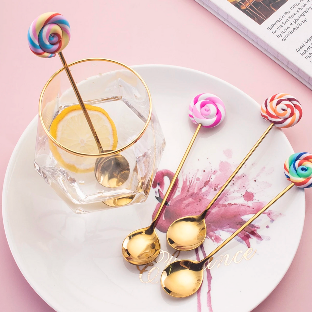 Gold lollipop-style cutlery with colourful swirly handles on a soft pink background