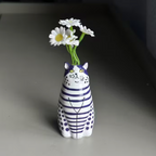 Close-up of a red and white striped cat-shaped bud vase held in a hand