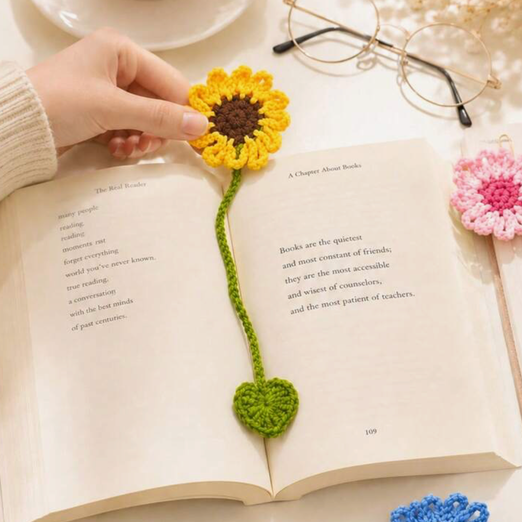 Yellow, blue and pink crochet flower bookmarks with green leaf ends beside an open book