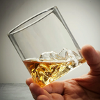 Mountain whisky tumbler filled with whisky beside a bottle and orange garnish