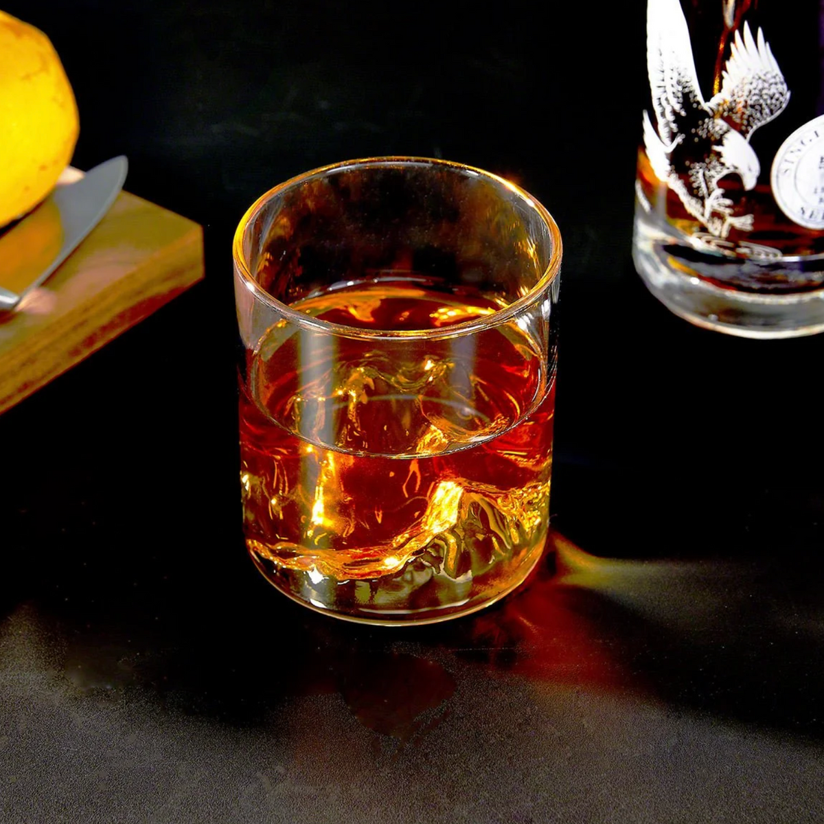 Whisky being poured into a mountain-inspired tumbler beside another glass