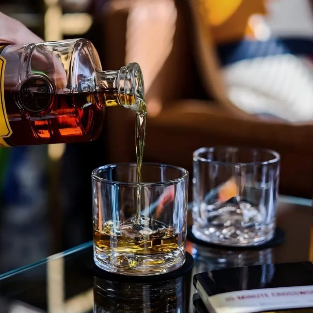 Hand holding a square mountain whisky glass filled with whisky and ice