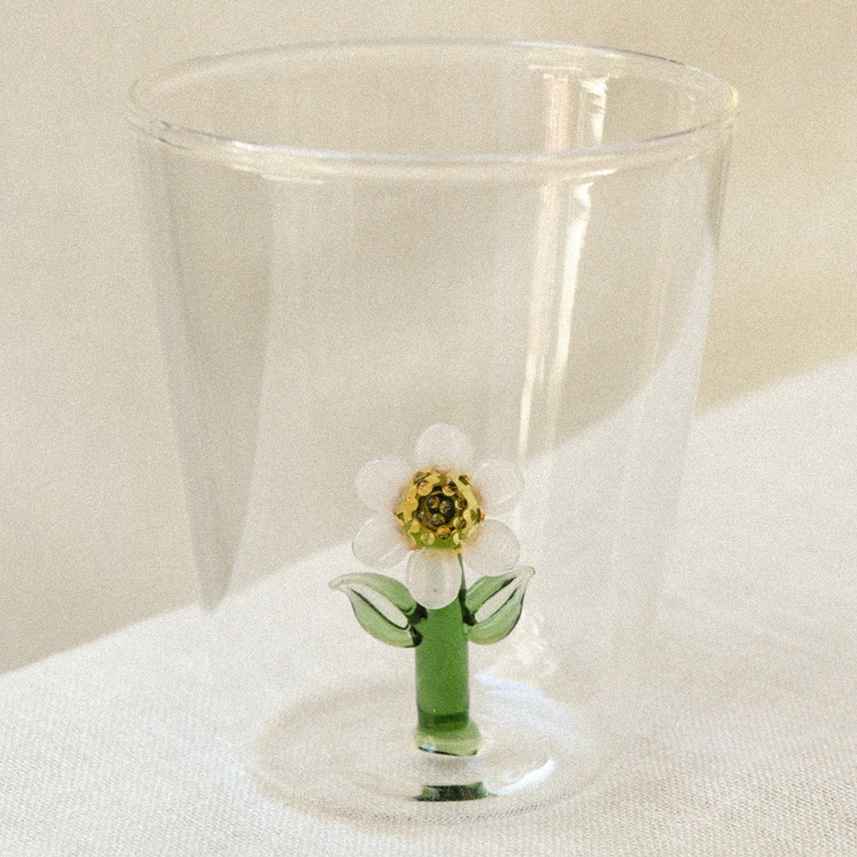 Two clear glass tumblers with a glass flower inside, on a wooden garden table