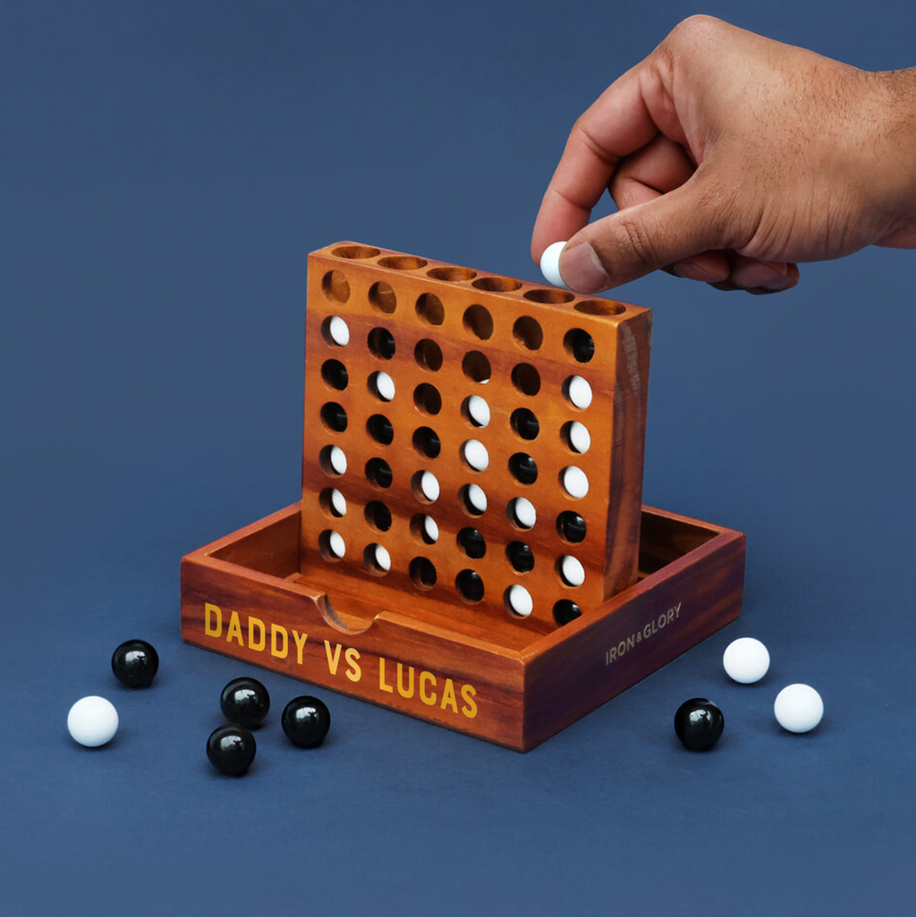 Personalised wooden Travel Four In A Row game with black and white marbles on a blue background