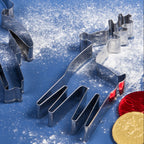 A set of metal holiday cookie cutters, including a reindeer and a penguin, arranged on a blue surface dusted with white flour, alongside wooden utensils with red handles and gold and red chocolate coins.