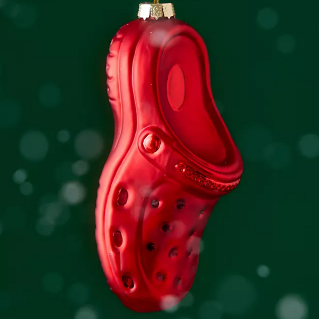 A glossy red clog-shaped Christmas ornament hanging against a dark green background with soft white bokeh lights.