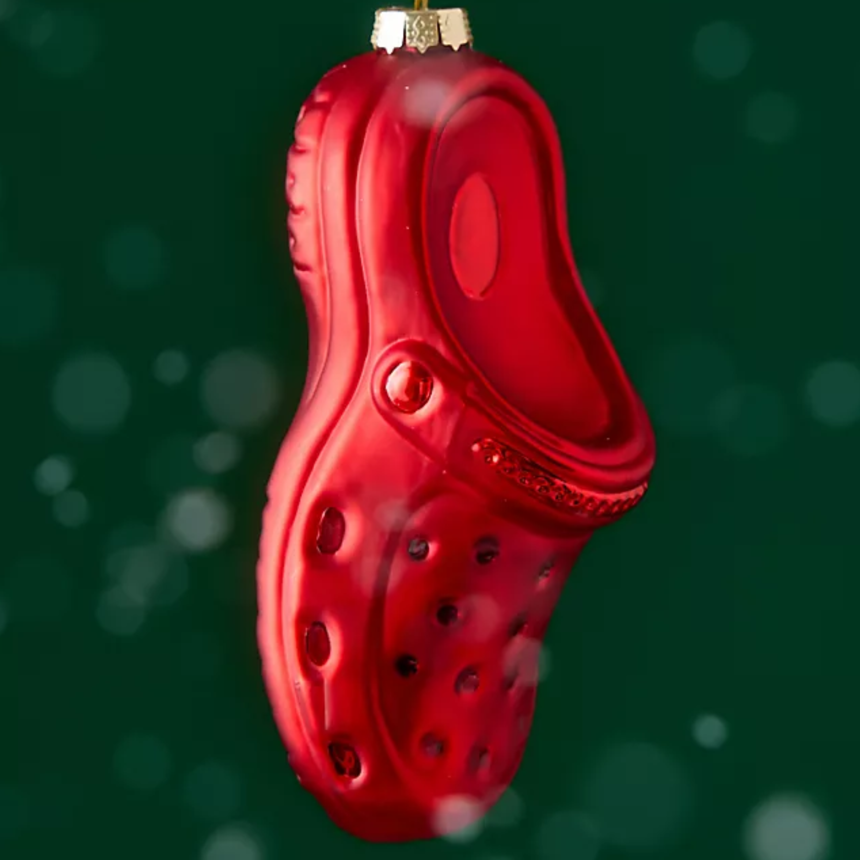 A glossy red clog-shaped Christmas ornament hanging against a dark green background with soft white bokeh lights.