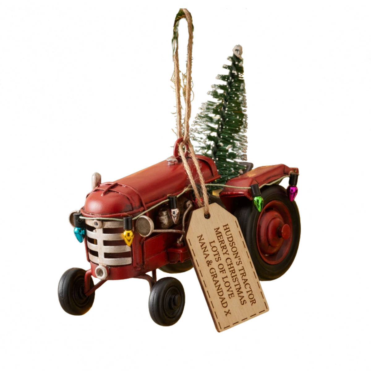 A red vintage tractor ornament with a hanging twine loop, a small green Christmas tree on top, colorful lights, and a personalized wooden tag that reads 'HISROY TRACTOR MRS. GUESTS MANY LOVES NANA & GRANDPA'.