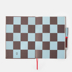 An open notebook with a brown and light blue checkerboard pattern cover, shown on a white background with a red ribbon bookmark and a pen tucked behind it.