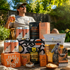 A curated snack and beverage assortment displayed on a wooden table in a backyard setting, with a man sitting in the background holding a drink. The products include cans of Full Circle Brew Co.