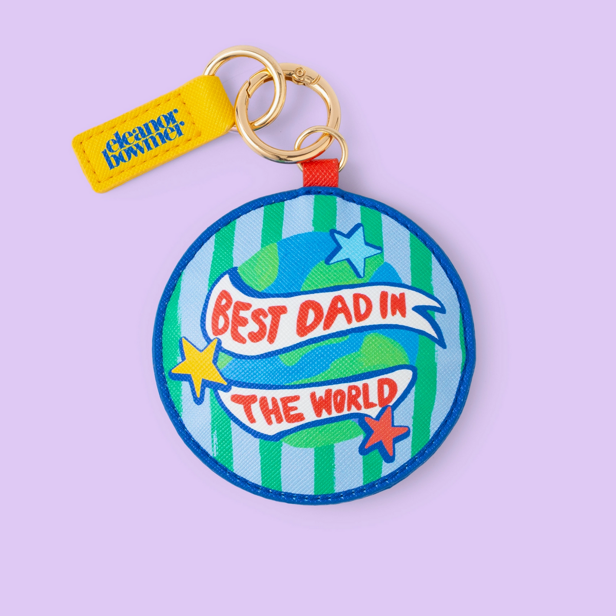 A round embroidered patch keychain by Cleaner Brown featuring a blue and green striped globe design with the text 'BEST DAD IN THE WORLD' in red, attached to a gold key ring and a yellow brand tag, set against a solid lavender background.