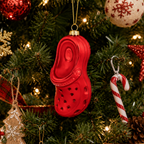 A red croc-heel-shaped Christmas ornament hanging on a decorated Christmas tree with lights, candy canes, snowflake ornaments, and other holiday decorations.