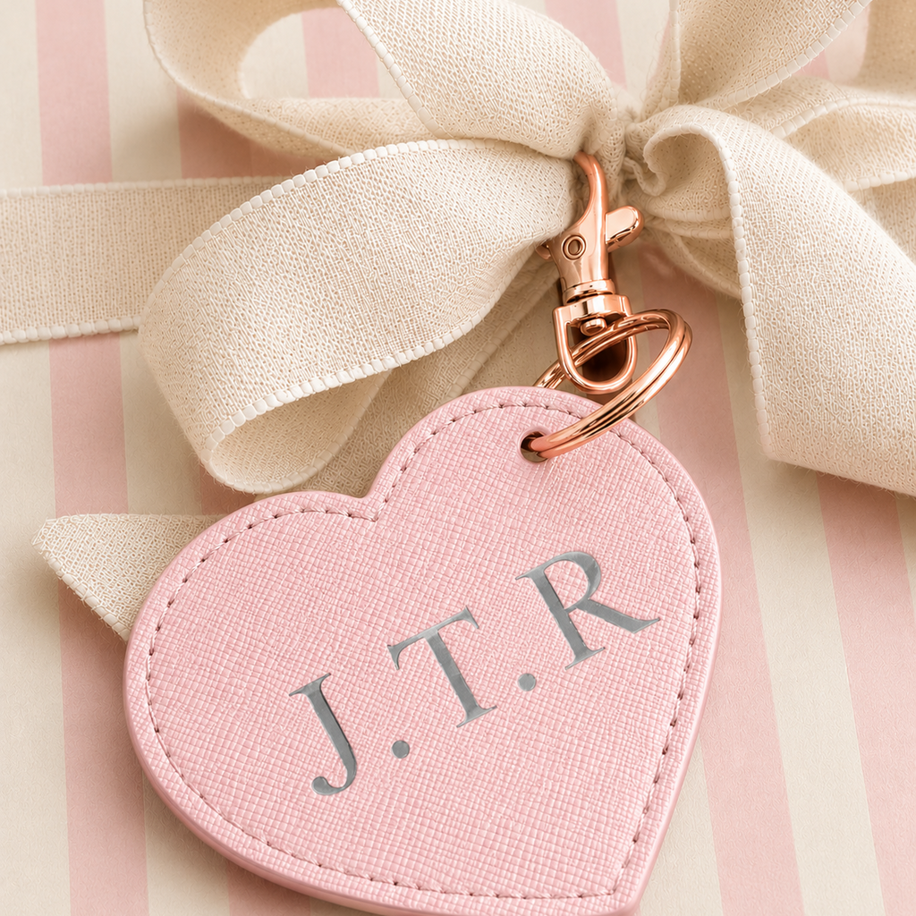 A pink heart-shaped leather keychain with silver-gray monogram letters 'J.T.