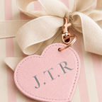 A pink heart-shaped leather keychain with silver-gray monogram letters 'J.T.