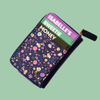 A zip-around wallet with a dark purple floral print and three colorful card slots labeled ISABELLE'S, SWEETIE, and MONEY, shown on a solid pale green background.