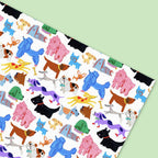 A square sheet of wrapping paper featuring a playful, colorful pattern of cartoon dogs in various breeds and colors on a white background, shown diagonally against a light green backdrop.
