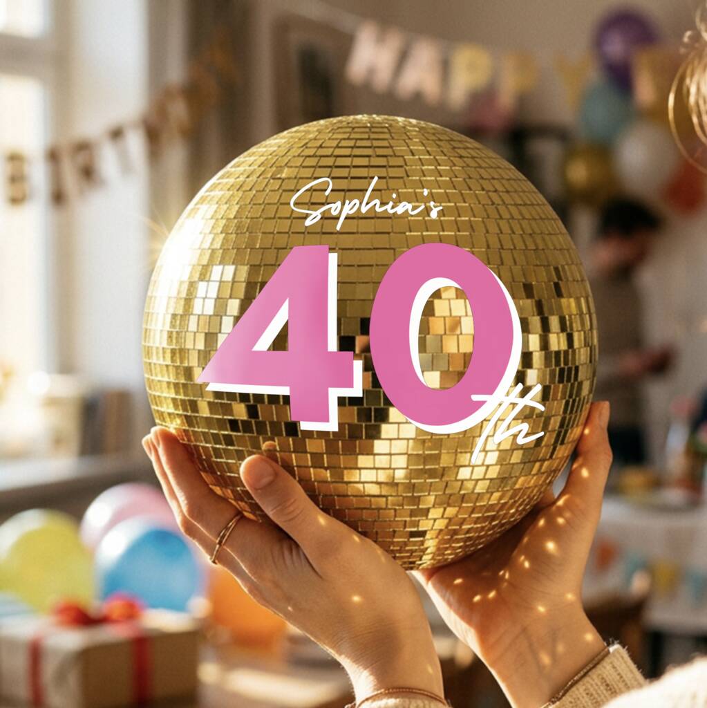 A person holds a gold disco ball decorated with pink and white text reading 'Sophia's 40th'. The background is a softly blurred birthday party room with balloons, gifts, and a 'HAPPY BIRTHDAY' banner.