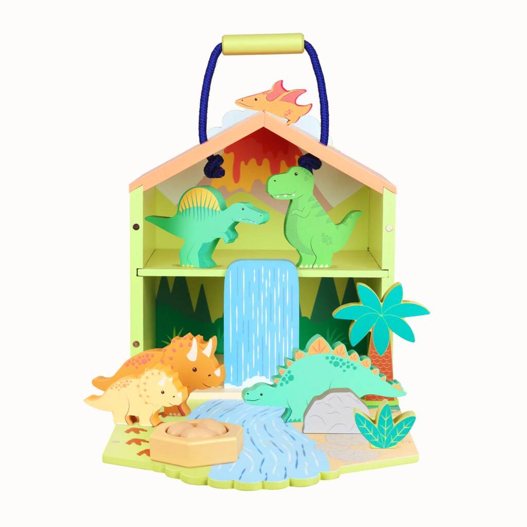 A wooden dinosaur playset in the shape of a house with a blue handle, featuring colorful dinosaur figures, a waterfall, palm trees, and a sandy ground on a white background.