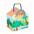 A colorful wooden house-shaped children's toy box with a dinosaur theme, featuring an illustrated prehistoric landscape with palm trees, a green T-Rex, an erupting volcano, and the text 'Oliver's Dinosaur'. It has a light green handle and a blue rope handle, shown on a plain white background.