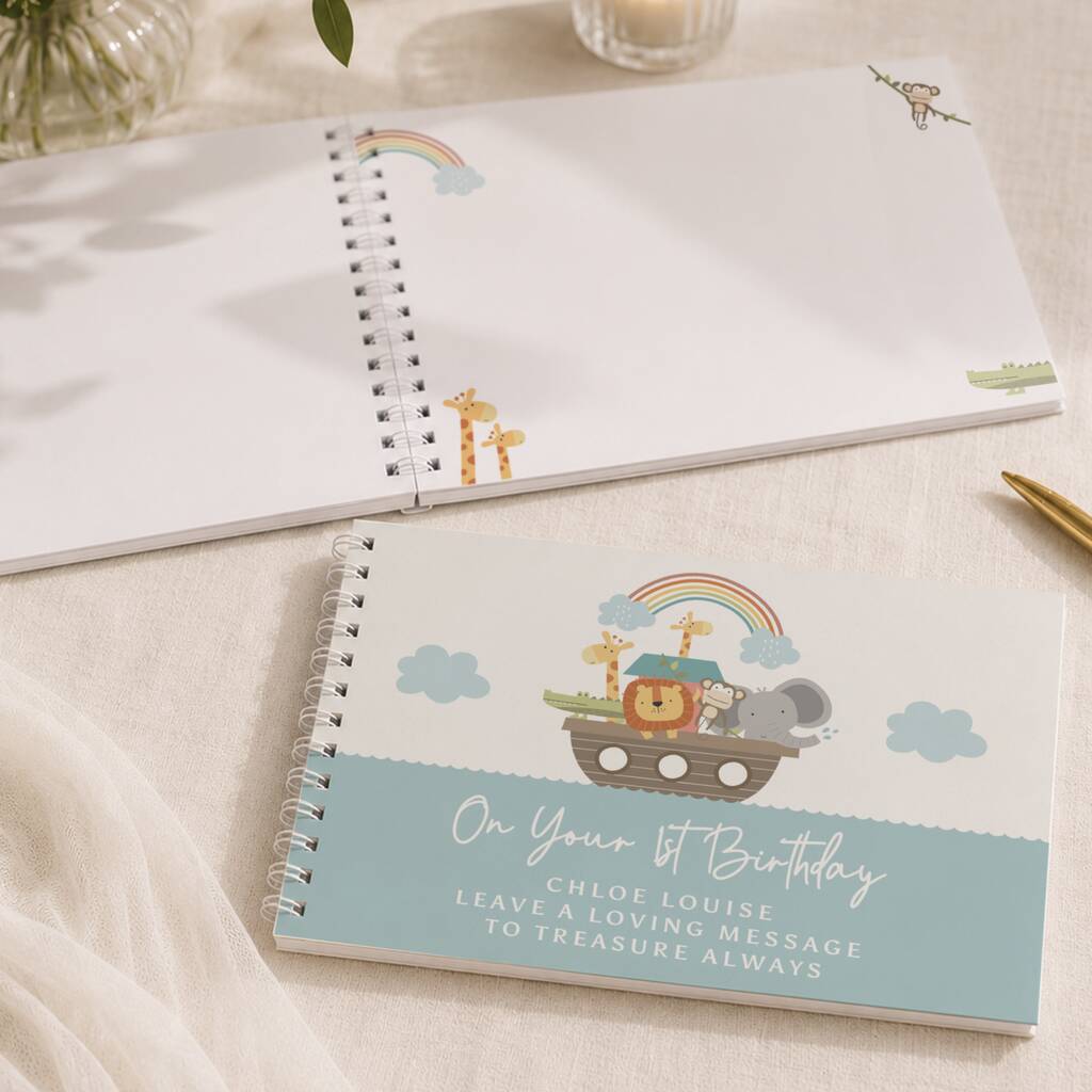 Two spiral-bound baby milestone notebooks on a beige fabric surface. The top notebook is open, showing blank white pages with small safari animal illustrations.