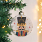 Clear Christmas ornament with a nutcracker design and 'Connor' text, hanging on a tree.