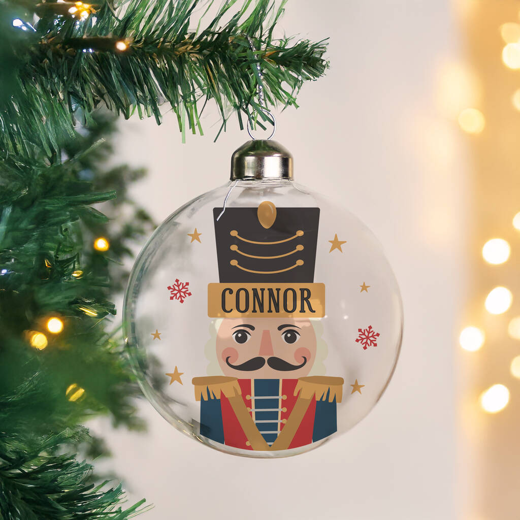 Clear Christmas ornament with a nutcracker design and 'Connor' text, hanging on a tree.