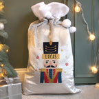 Personalized Christmas sack with a nutcracker design and the name 'Lucas', placed against a festive background with lights and a tree.