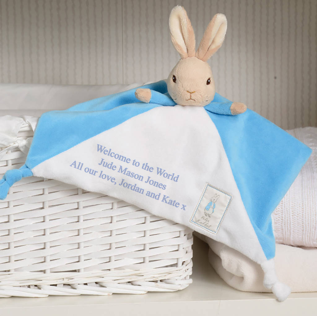 Personalised Peter Rabbit baby comforter in blue and white with embroidered welcome message, draped over a white basket