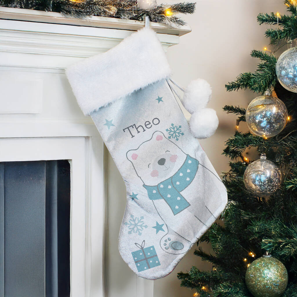 Personalized Christmas stocking with a bear design hanging by a fireplace next to a decorated tree.