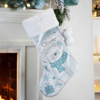 Personalized Christmas stocking with a bear design hanging by a fireplace.