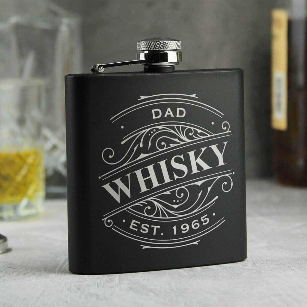Black flask with 'Grandad's Whisky Est. 1960' engraving on a blurred background