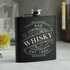 Black flask with 'Grandad's Whisky Est. 1960' engraving on a blurred background